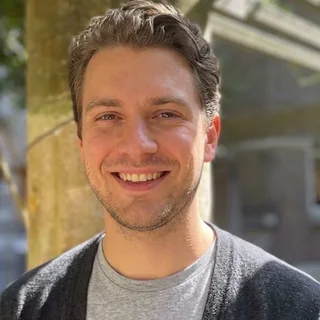 Sander Groen photographed outdoors in daylight in a grey cardigan over a grey t-shirt, smiling at the camera.